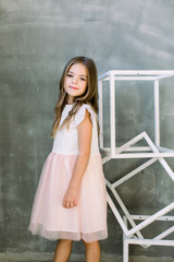 Beautiful little girl with broun long hair on a grey background near the white constructure of the...