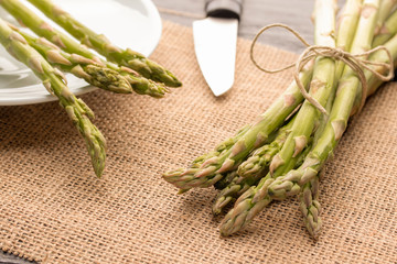 Fresh green asparagus on the table and in a white plate with a shiny knife.