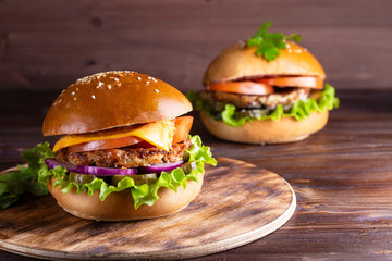 two homemade hamburgers with beef and cucumbers on wooden background