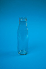 Transparent empty glass bottle with a wide neck on a blue background.