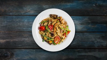 Rotating udon stir fry noodles with with seafood in a white plate on wooden background. Top view
