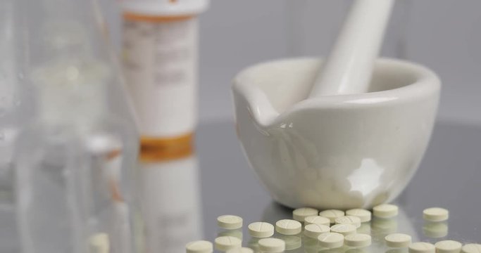 Rx mortar and pestle with pills rotating on a mirror with bottles and beakers