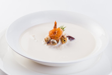 Fresh Creamy seafood soup with shrimps on a white plate on a light background (close)