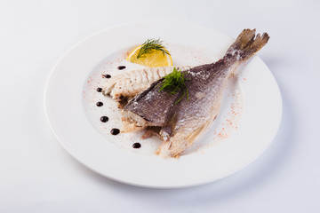grilled dorada in salt with lemon slice on a white plate on a light background (close)