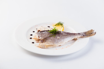 grilled dorada in salt with lemon slice on a white plate on a light background (close)