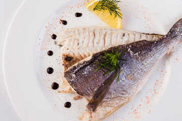grilled dorada in salt with lemon slice on a white plate on a light background (close)