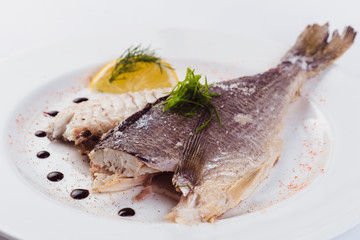 grilled dorada in salt with lemon slice on a white plate on a light background (close)