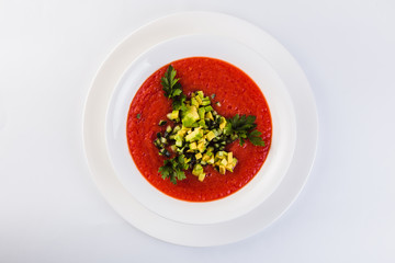 Spanish soup gazpacho with avocado and cucumber on a white plate on a light background (close top view)