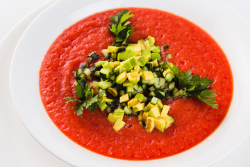 Spanish soup gazpacho with avocado and cucumber on a white plate on a light background (close)