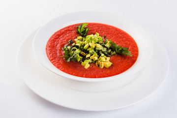 Spanish soup gazpacho with avocado and cucumber on a white plate on a light background (close)