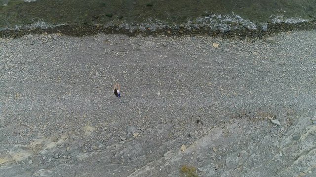 Woman is doing squats the bodyflex on the sea stone beach. Aerial beautiful footage top view.