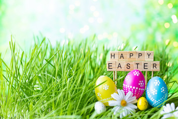 Phrase Happy Easter made of letters on a background of green grass, Easter eggs.