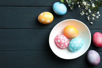 Plate with colorful easter eggs and flowers on wooden background. Festive tradition. Space for text. Top view