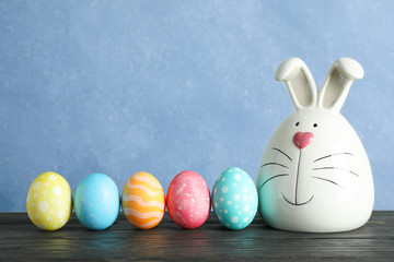 Decorated bunny and Easter eggs on table against color background. Space for text