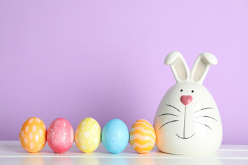 Decorated bunny and Easter eggs on table against color background. Space for text