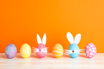 Decorated Easter eggs and cute bunny's ears on table against color background. Space for text