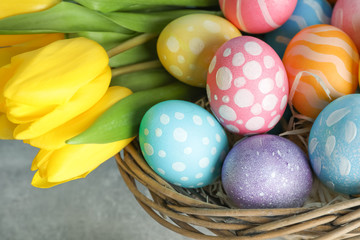 Fototapeta na wymiar Easter basket filled with colorful eggs and flowers on a wooden background. Close up