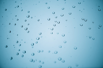 Window glass with drops of rain. Atmospheric mint blue aqua light background with raindrops. Azure droplets close up. Detailed transparent aquamarine texture in macro with copy space. Rainy weather.