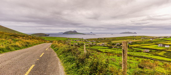 Empty road leading to village, coastline and islands in a distance, moody dark sky with stormy clouds