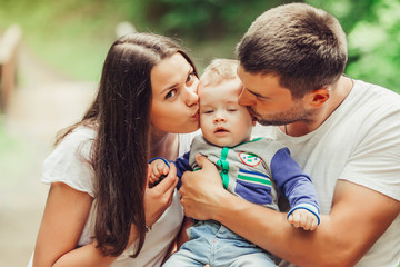 Happy loving young family with infant baby walking together in green summer park hugging each other. Family, togetherness, childhood concept