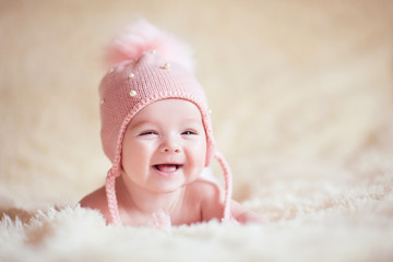 Happy baby girl wearing stylish knitted hat lying in bed close up. Childhood. - obrazy, fototapety, plakaty