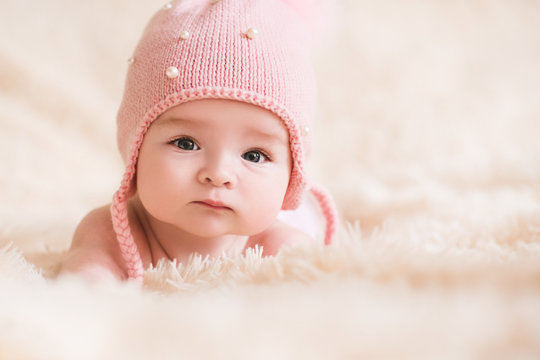 Cute baby girl wearing knitted hat lying in bed closeup. Looking at camera. Childhood.
