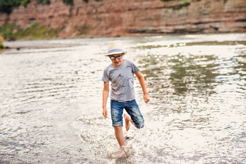 Blonde smiling boy with strabismus playing on the river