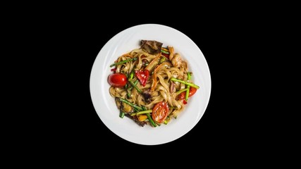 Rotating udon stir fry noodles with seafood and vegetables isolated on ablack background. Top view