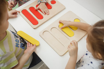 Toddlers playing multicolored educational games, mosaic and puzzles table.
