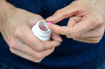 Close-up of man holding prescription bottle with pink pills in his hand.Concept of an old man trying to get his medicine.
