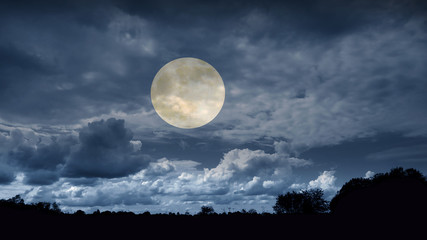 Full mystical Moon in the clouds above the forest. Landscape of night nature at sunset. 