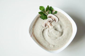 Mushroom soup puree in a plate with greens on a white background