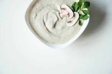 Mushroom soup puree in a plate with greens on a white background