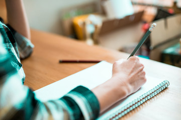 Close up of woman's hands writing in spiral notepad placed on wooden desktop