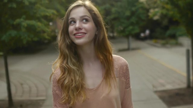 Young Woman Enjoys Walking Through Park, She Receives A Text And Smiles/Laughs