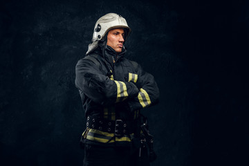 Manly firefighter in helmet looks sideways in studio on black background