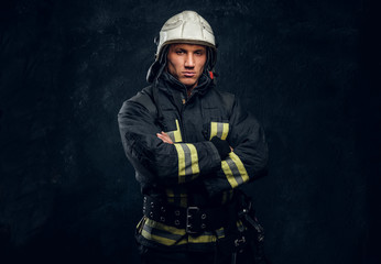 Manly firefighter in helmet looks into camera in studio on black background