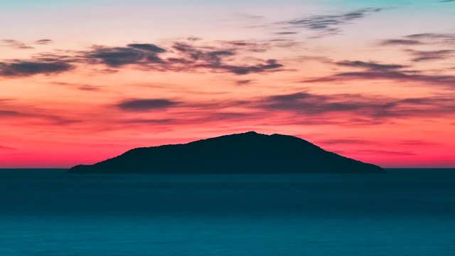 Timelapse video of a small island silhouette in the middle of the sea at sunrise, Colorful sky with red, cyan and blue tones. Day rising. Ilha do Arvoredo - Bombinhas SC, Brazil.