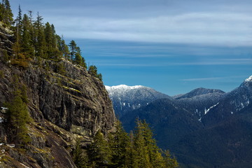 Winter forest in the mountains over Vancouver and snow-capped   peaks on  the background of  blue cloudy sky. The picture was taken from the cabin of the sky ride going to the ski slopes of the Grouse