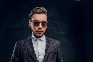 Fototapeta premium An elegantly dressed young man in sunglasses against a dark textured wall