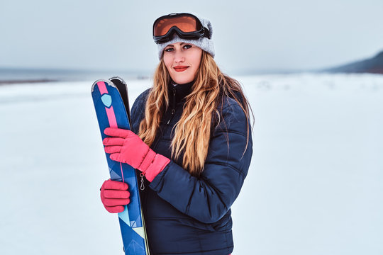 Charming Norwegian woman wearing warm clothes posing with skis on a snowy beach