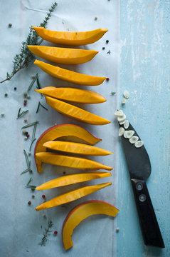 Sliced Hokkaido pumpkin and garlic with herbs on wood