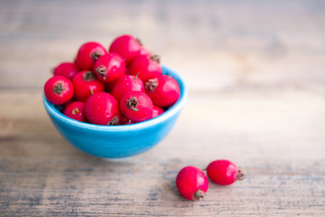 Hawthorn tincture in a blue small bowl and fresh hawthorn fruit on the wooden surface of the table. Herbal medicine. Selective focus.