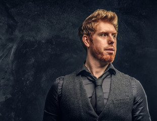 Portrait of a handsome redhead man dressed in elegant vest and tie in studio against a dark textured wall