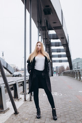 Young blondie sexy sensual girl go across the bridge in black coat. Outdoor portrait. Casual, lifestyle concept