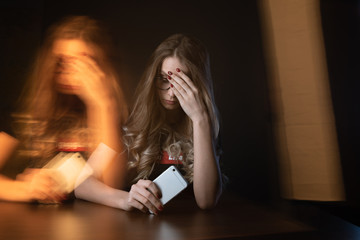 Closeup picture of frustrated girl, young woman being a victim of bullying online sitting isolated over the black backgrownd