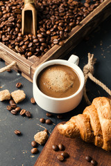 Black fried coffee beans in cafe with cookie and cake on dark textured background