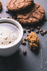 Black fried coffee beans in cafe with cookie and cake on dark textured background