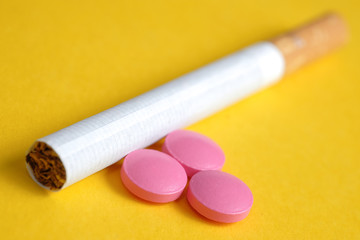 Pink pills for nicotine addiction lies next to a cigarette on a yellow background.
