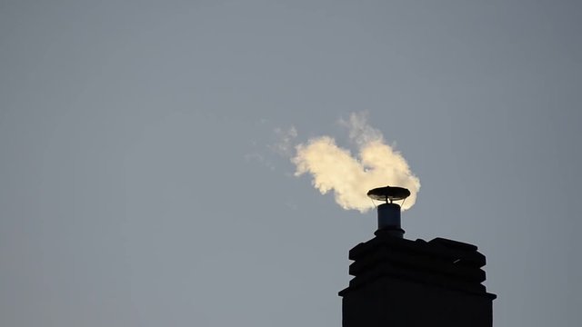 Footage of a chimney of the condominium heating system. The low rays of the winter sun enhance the puffs of smoke that increase and decrease depending on the engagement of the boiler.